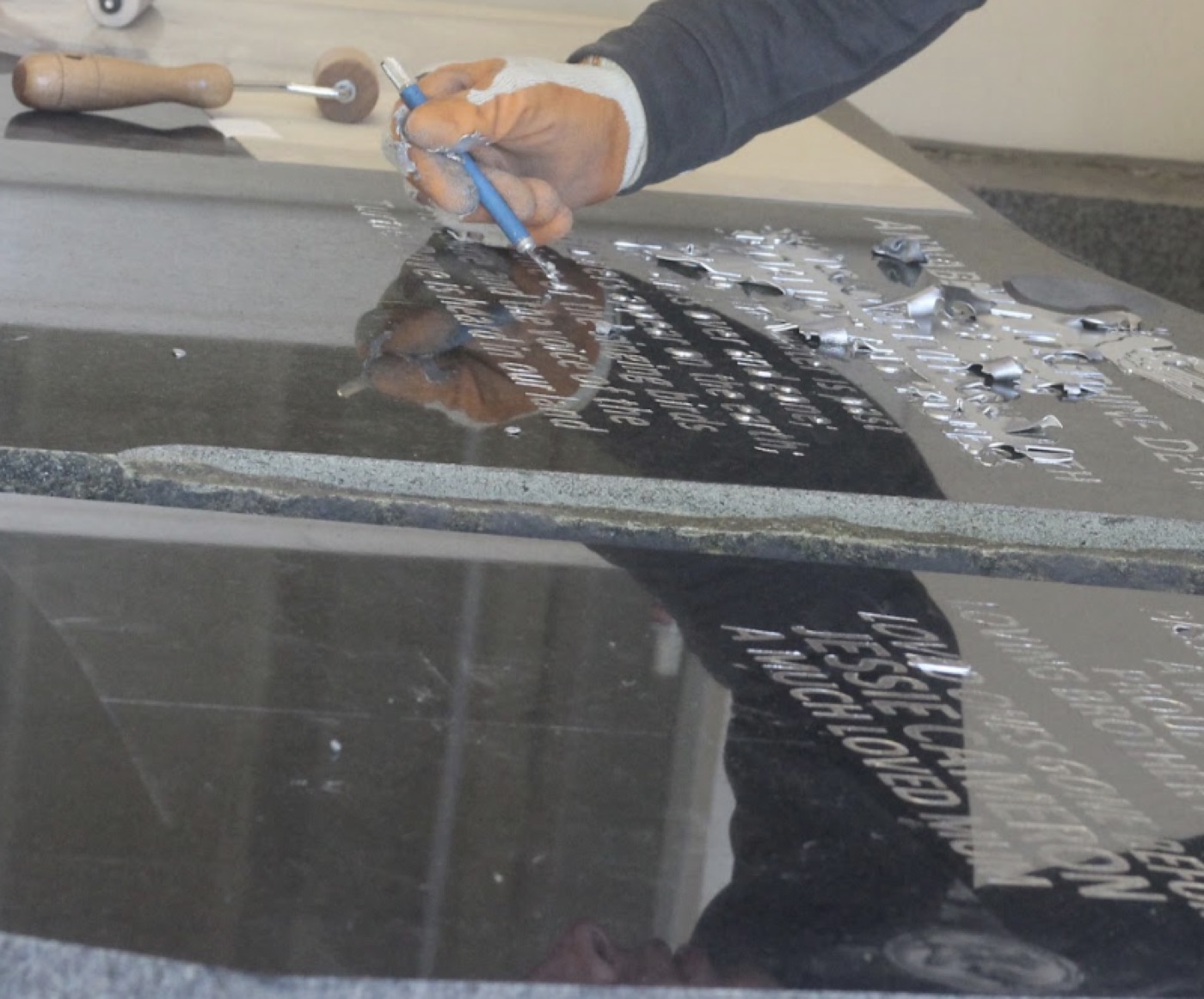 A mason hand lettering an inscription on a granite headstone