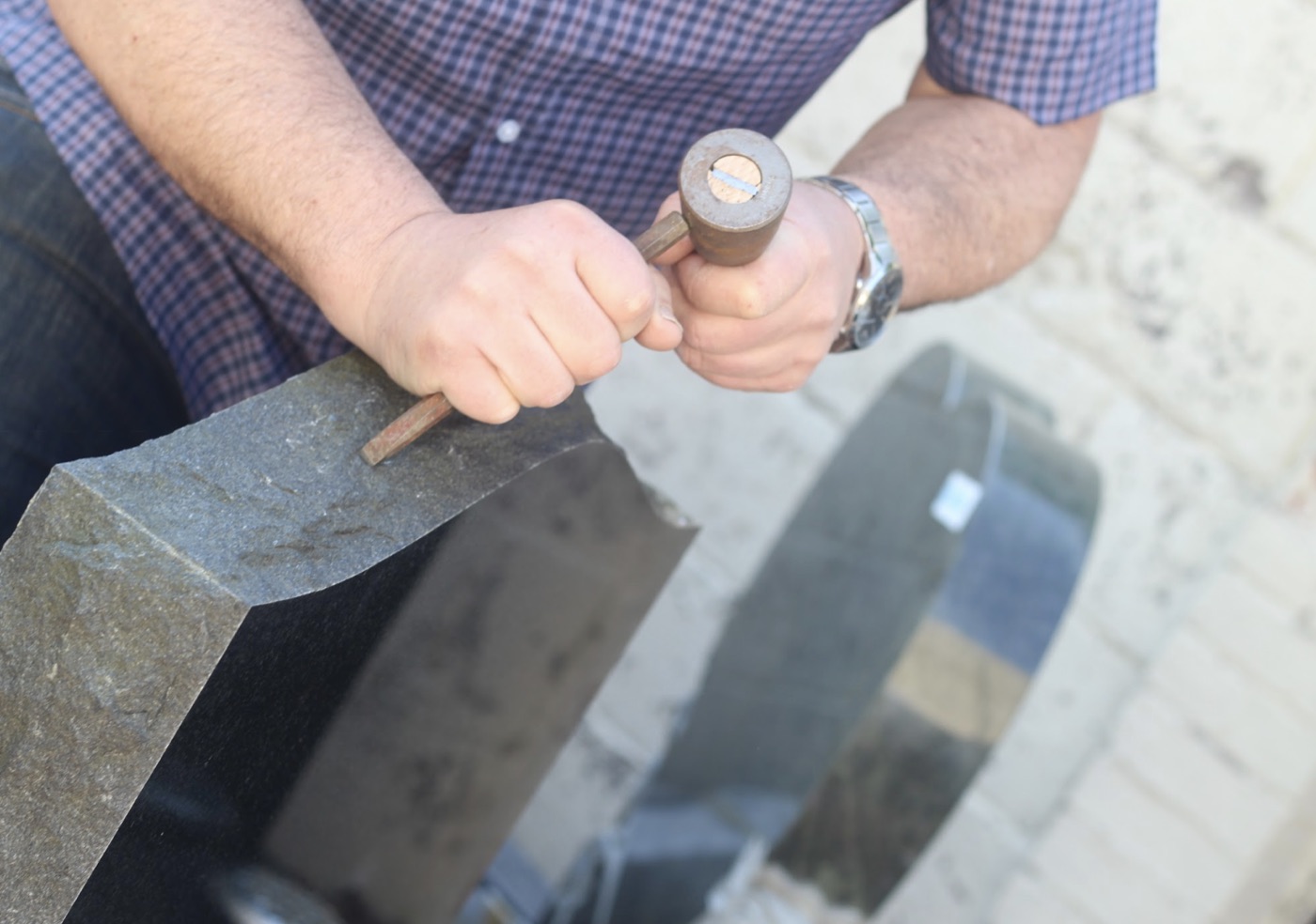 Memorial mason working the edge of a granite headstone at the yard