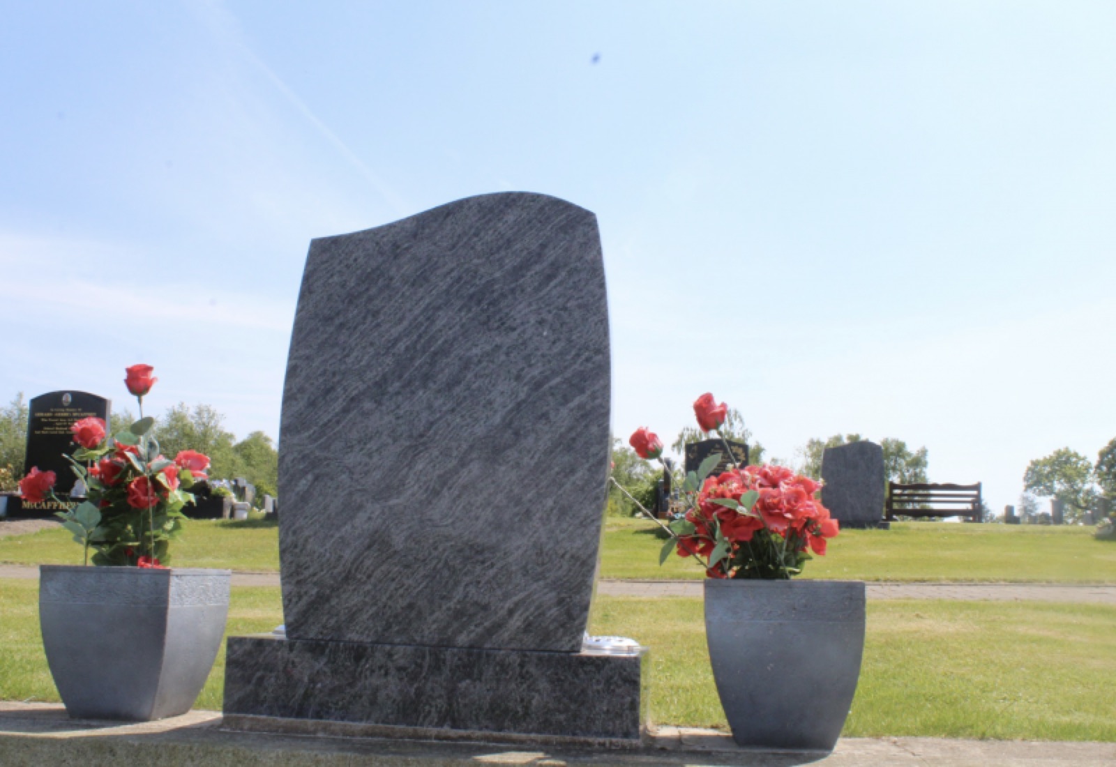 Vizac Blue granite headstone flanked by rose-filled granite vases